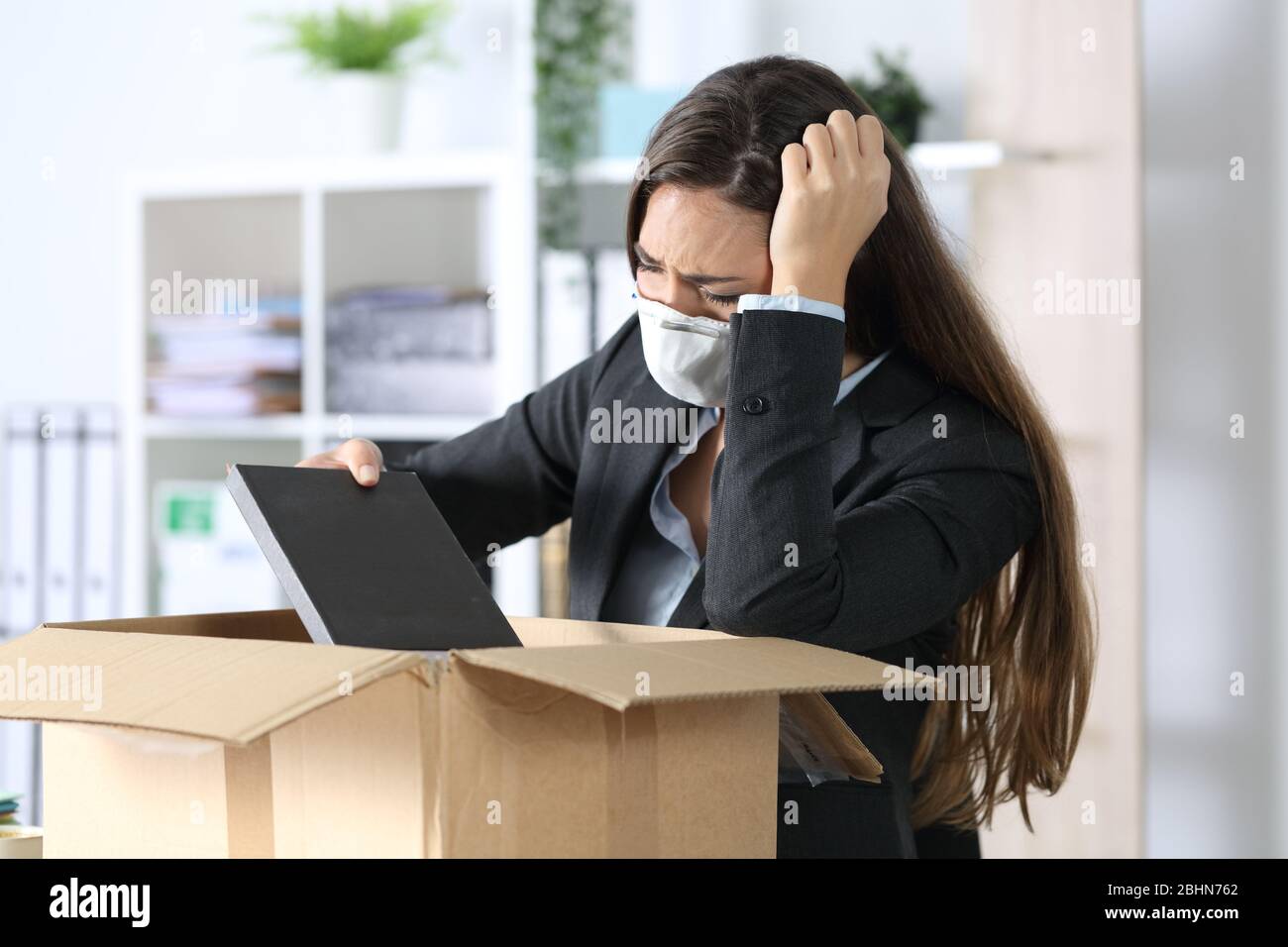 Sad fired executive woman with protective mask packing personal belongings on a box at the office Stock Photo