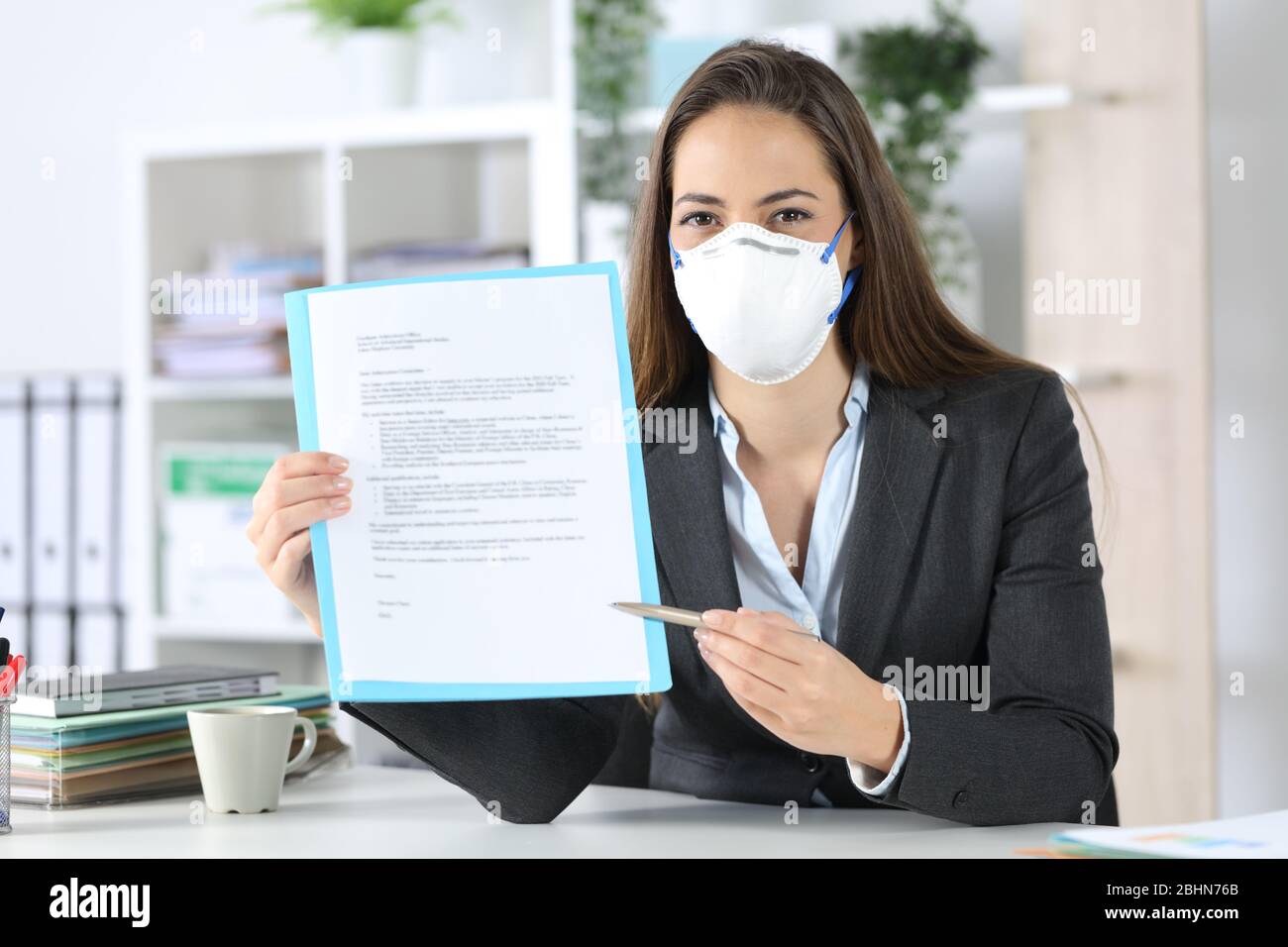Front view of executive woman wearing protective mask showing contract looking at camera at the office Stock Photo