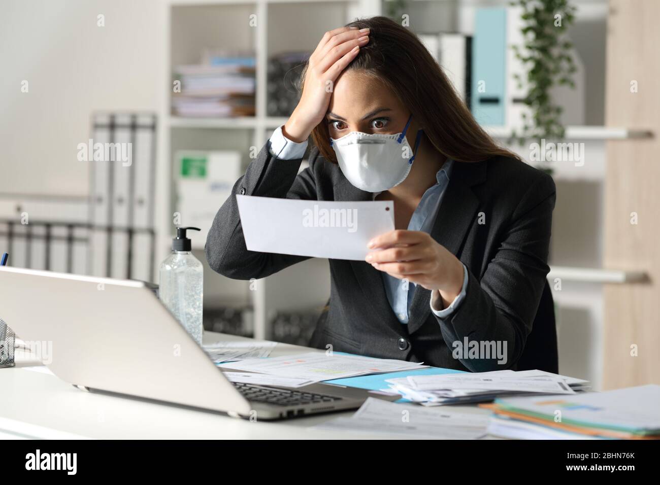 Surprised executive woman with protective mask looking at bank receipt at the office Stock Photo