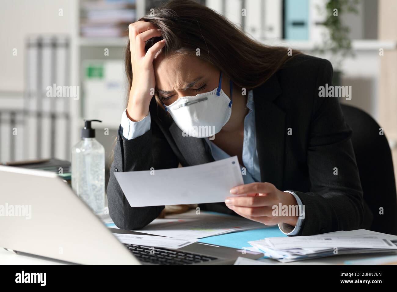 Sad executive woman with protective mask complaining looking bank receipt at the office Stock Photo