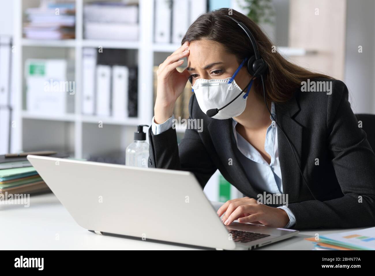 Worried telemarketer with protective mask looking at bad news on laptop in the office Stock Photo