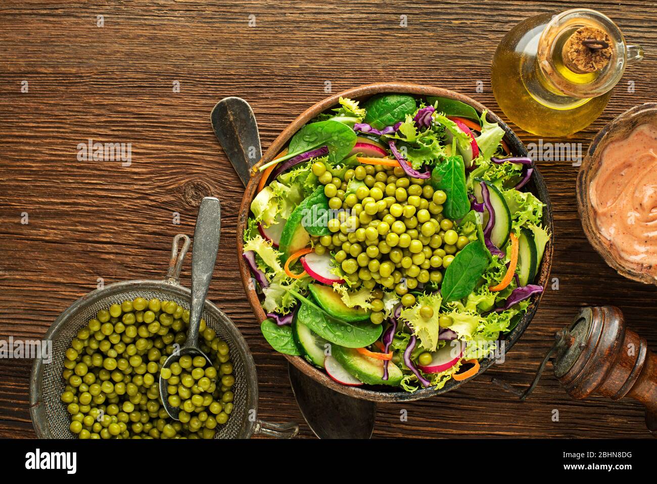 Green lettuce salad meal with fresh vegetables and peas on wooden table background Stock Photo