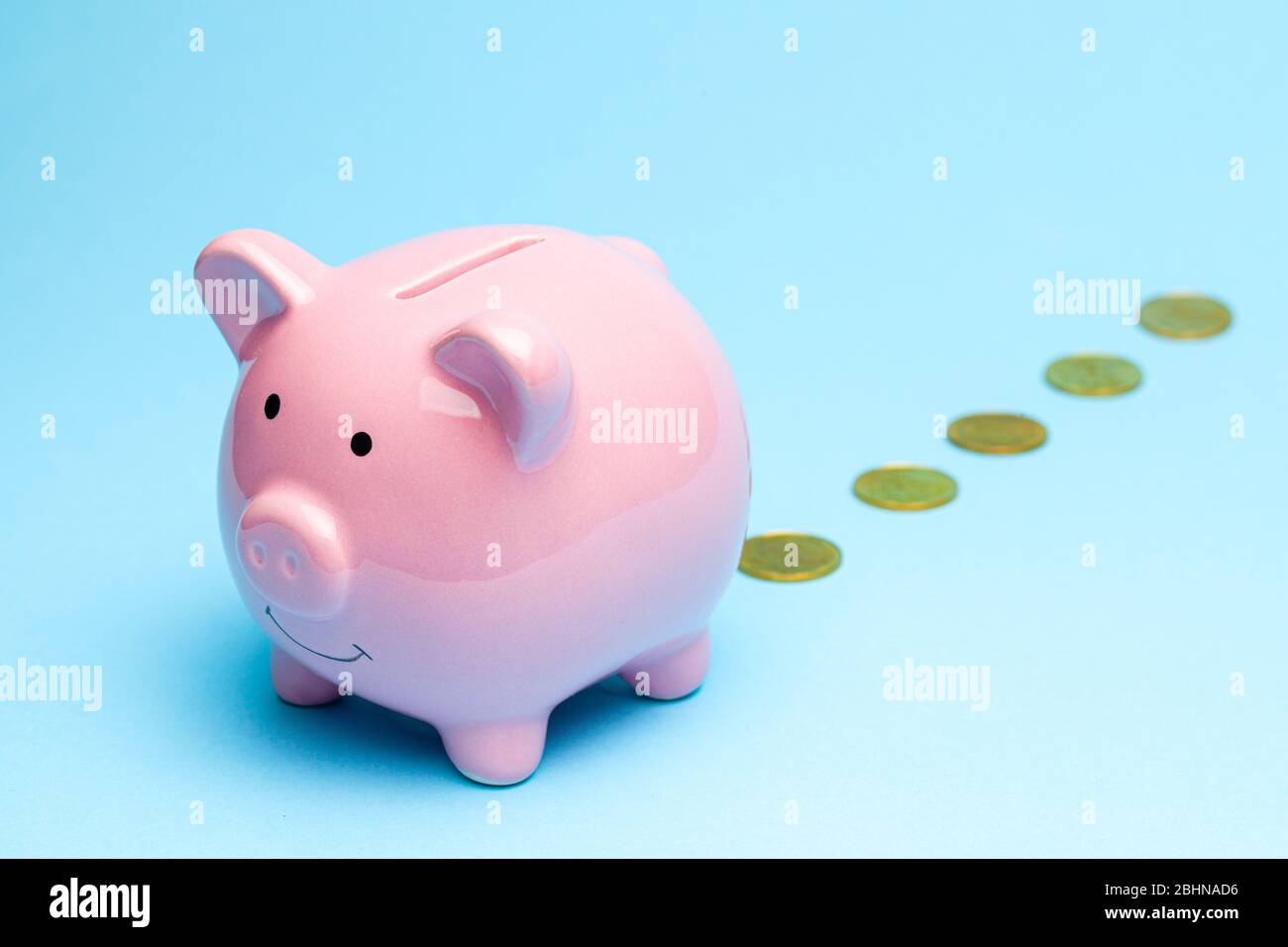 Loss of money. Pink piggy bank losing gold coins on blue background. Bad investment or falling profits. Stock Photo