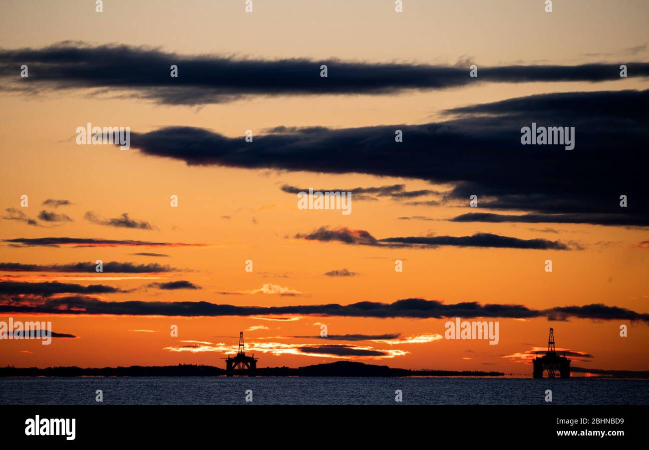 The sun rises behind redundant oil platforms moored in the Firth of Forth near Kirkcaldy, Fife. Stock Photo