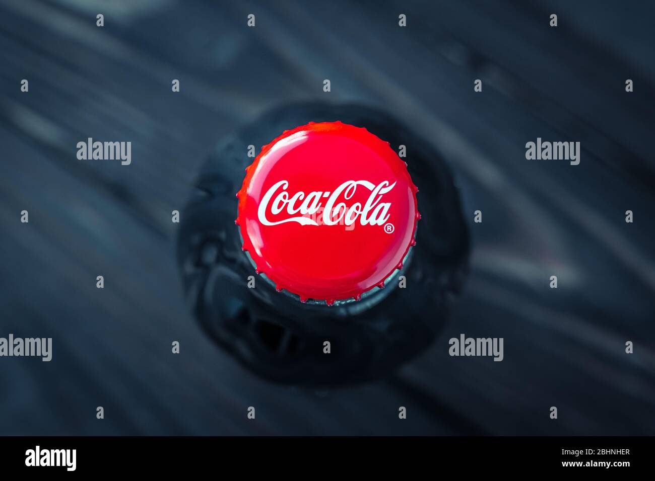 Kharkiv, Ukraine, April 26, 2020: A glass bottle of coca-cola on dark background. Close-up red cork of drink, top view. Illustrative editorial Stock Photo