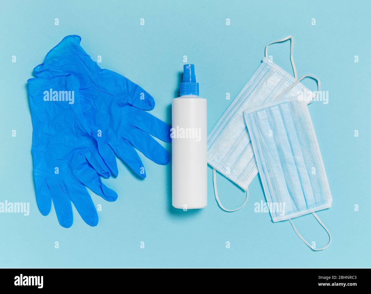 Coronavirus protection. Medical surgical mask, disinfectant or hand sanitizer and disposable gloves on blue background. Hygiene measures to prevent sp Stock Photo