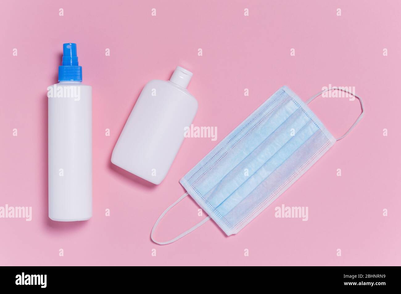 Coronavirus protection. Medical surgical mask and two bottles of disinfectant and alcohol hand sanitizer on pink background. Hygiene measures to preve Stock Photo