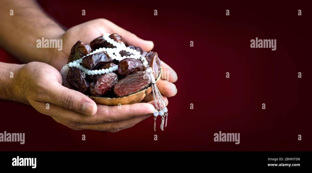 Hand with dates isolated red background, iftar concept islamic image Hands holding a golden color bowl of dates with Tasbeeh Stock Photo