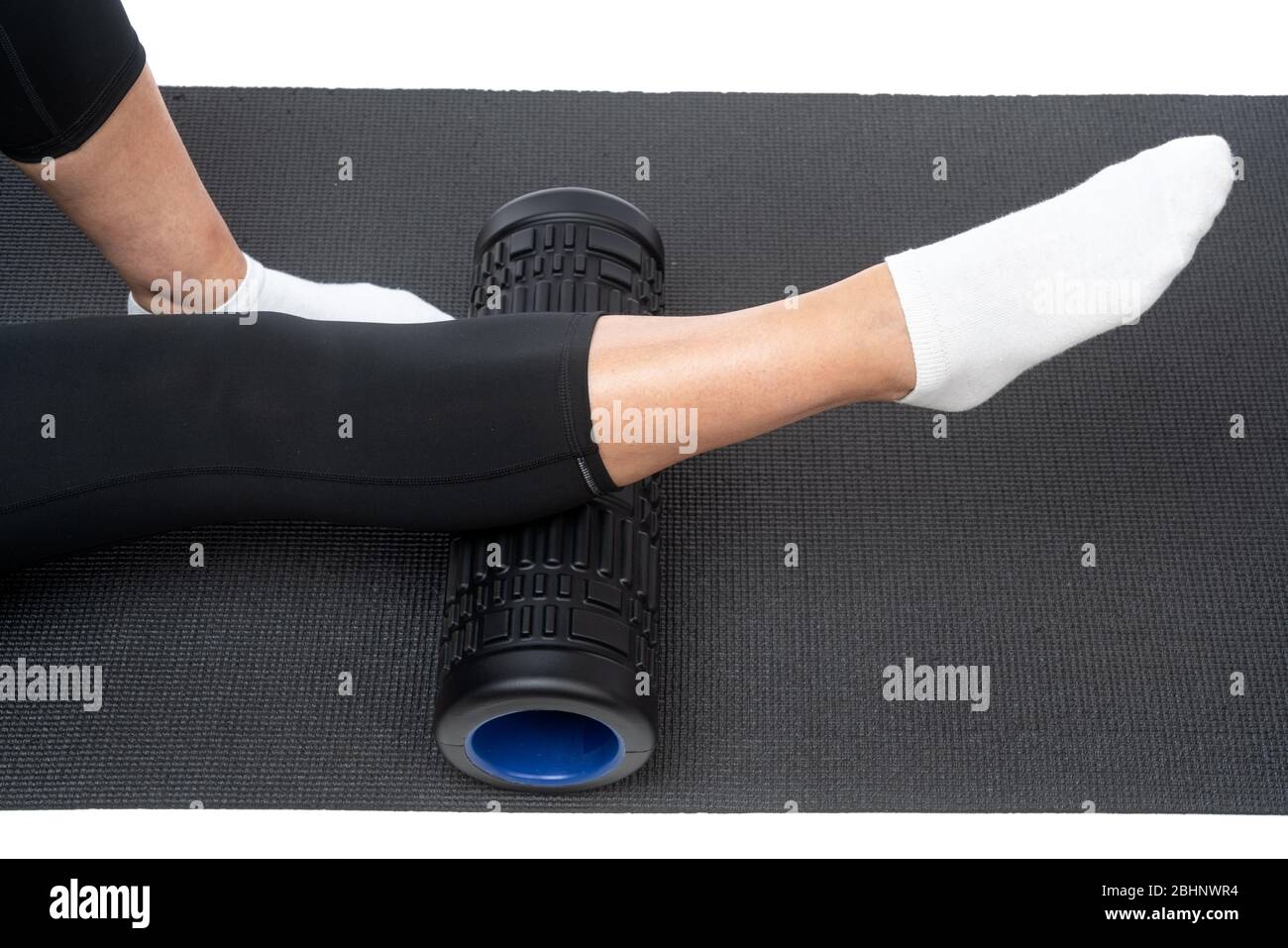 A middle-aged woman on a myofascial roller does a leg shin massage on a white background. Stock Photo
