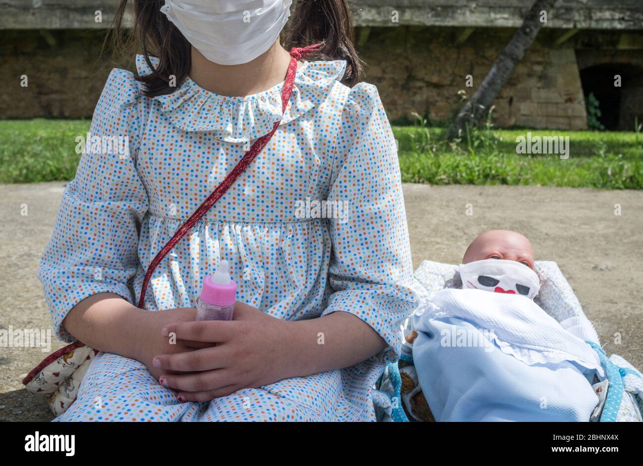 Little girl happy in her first day of children outing cause relaxation of confinement measures. SHe and her reborn doll are wearing face mask Stock Photo