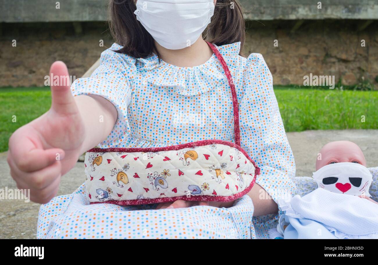 Little girl happy in her first day of children outing cause relaxation of confinement measures. SHe and her reborn doll are wearing face mask Stock Photo