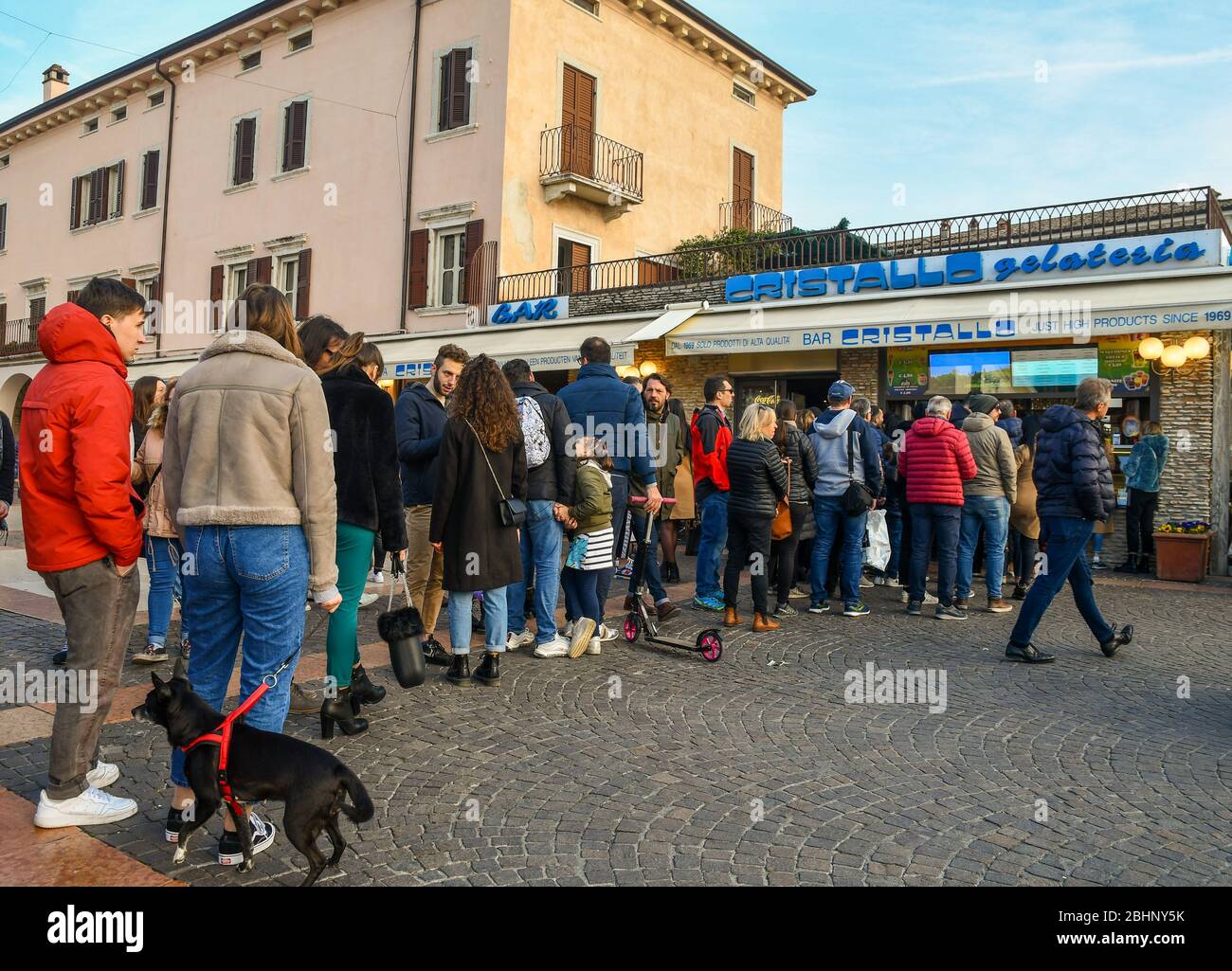 A lot of people standing in line waiting to buy ice cream outside an ice cream shop in the old town of Bardolino, Lake Garda, Verona, Veneto, Italy Stock Photo