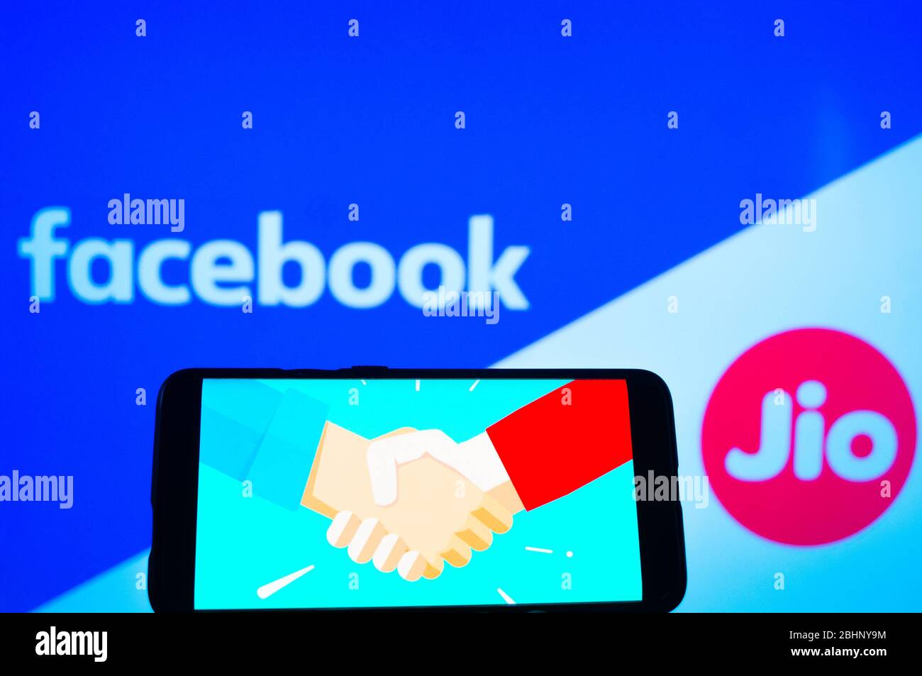 Jaipur, India, Circa 2020 - Photograph of a mobilephone with a handshake, signifying a deal, with facebook and Reliance jio in the background Stock Photo