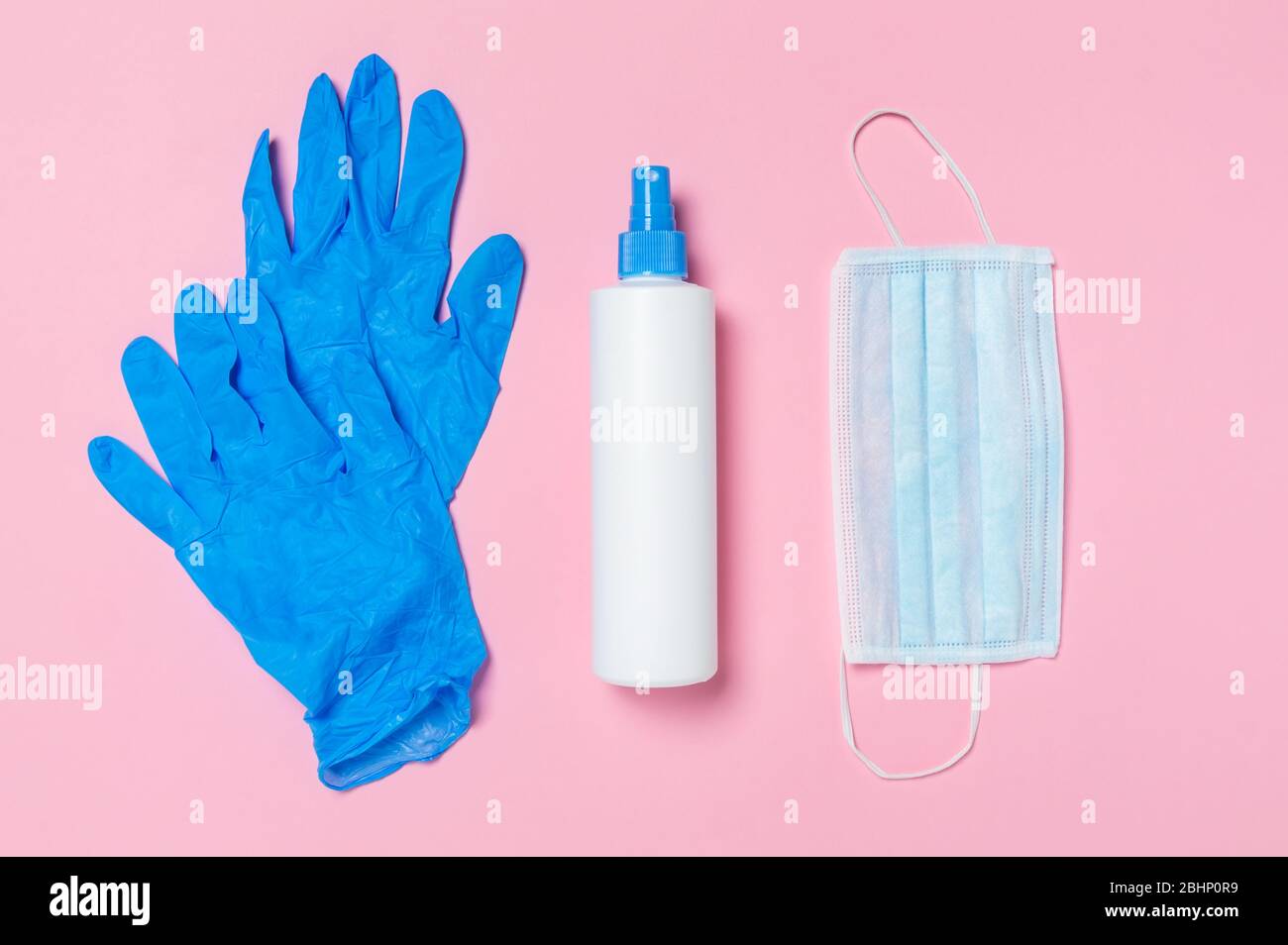 Coronavirus protection. Medical surgical mask, disinfectant or hand sanitizer and blue disposable gloves on pink background. Hygiene measures to preve Stock Photo