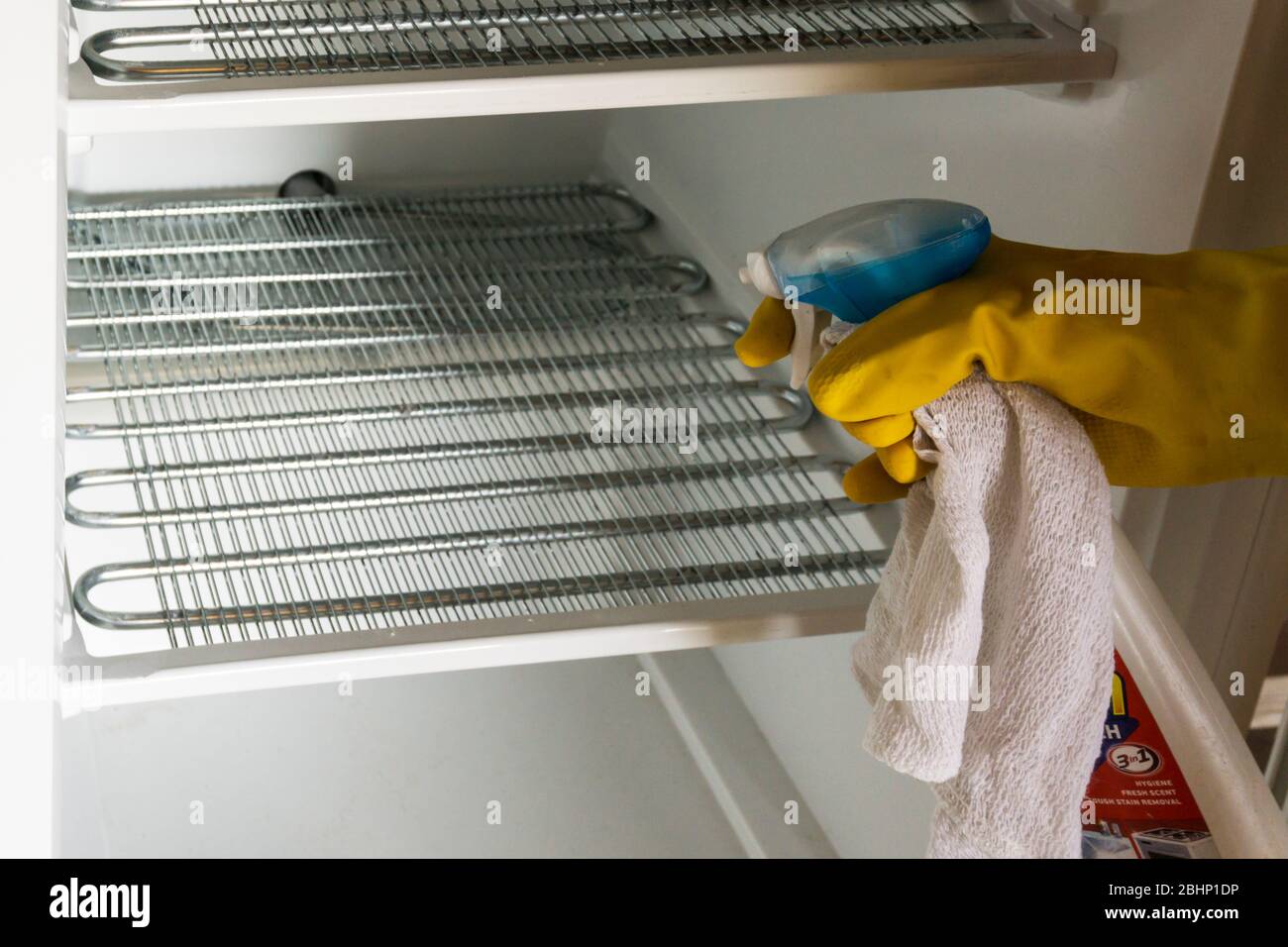 Cleaning the shelves of an empty freezer with a bleach disinfectant spray - spring cleaning. Stock Photo