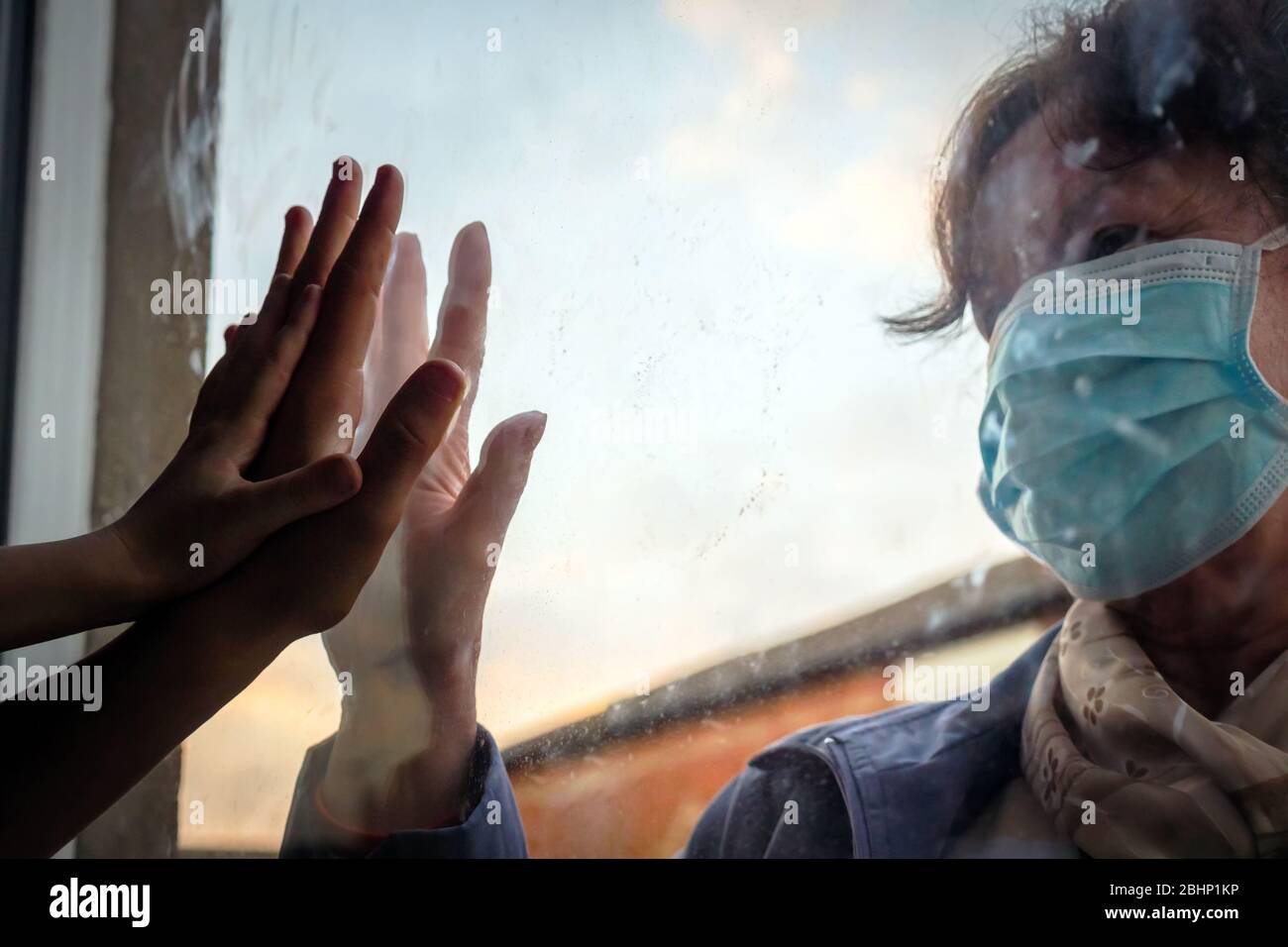 social distancing among the family, hand of the woman and her grandchildren on window plane, concept coronavirus and covid-19 pandemic Stock Photo