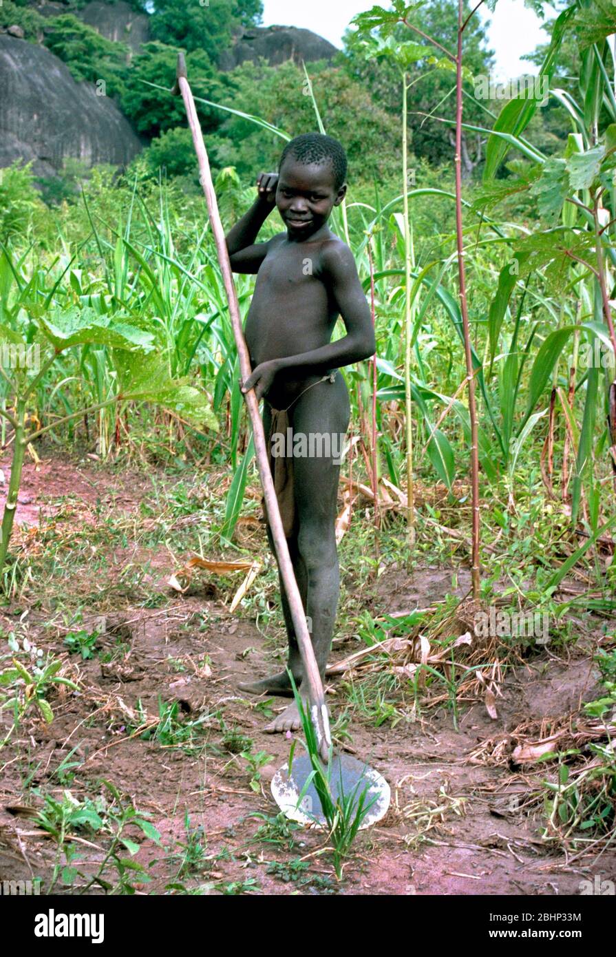 Sudanese boy using a hoe to farm the land in a remote village in Southern Sudan Stock Photo