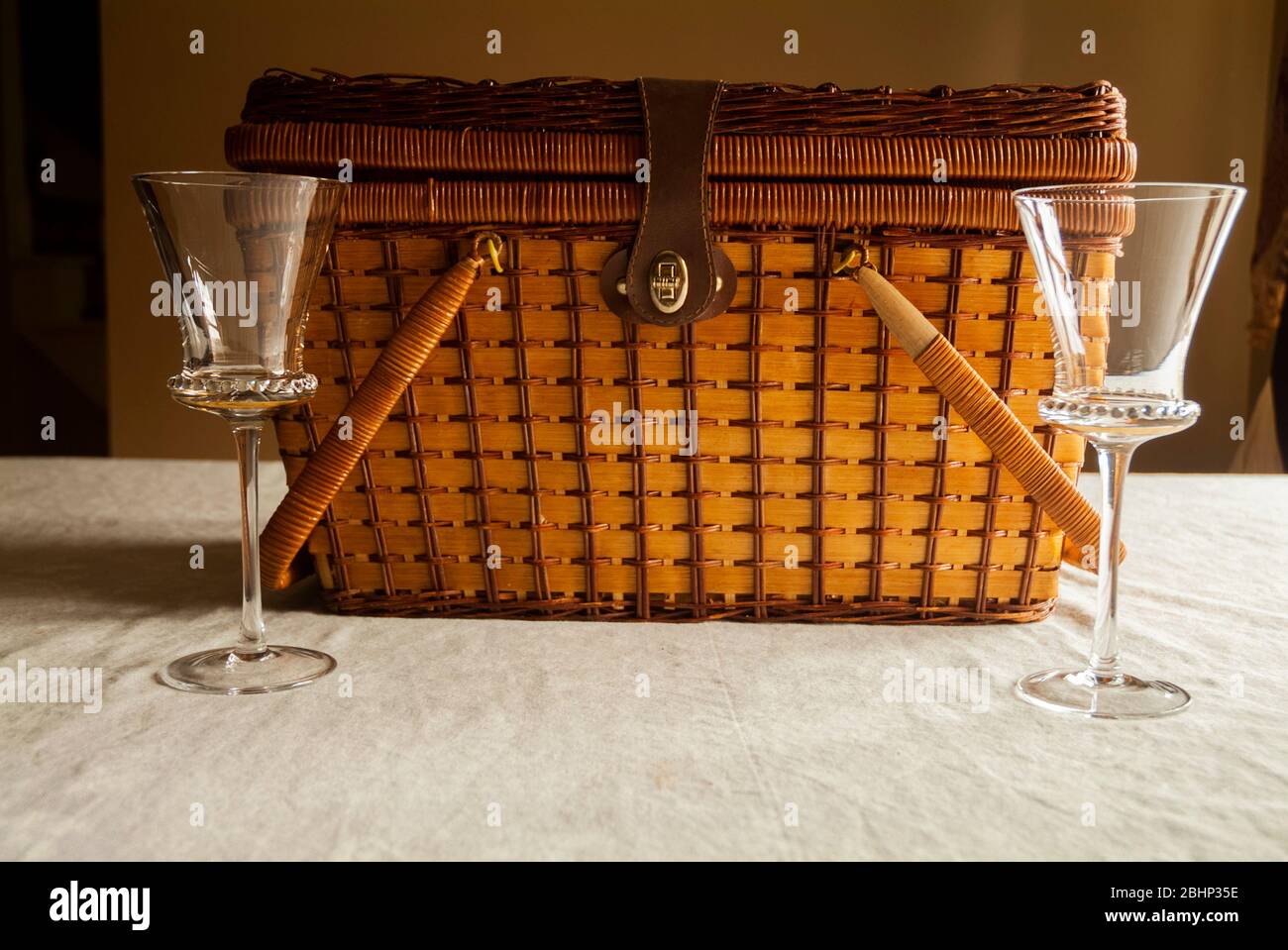 DATE NIGHT: Two wine glasses stand side by side in front of a picnic basket on a kitchen table. Stock Photo