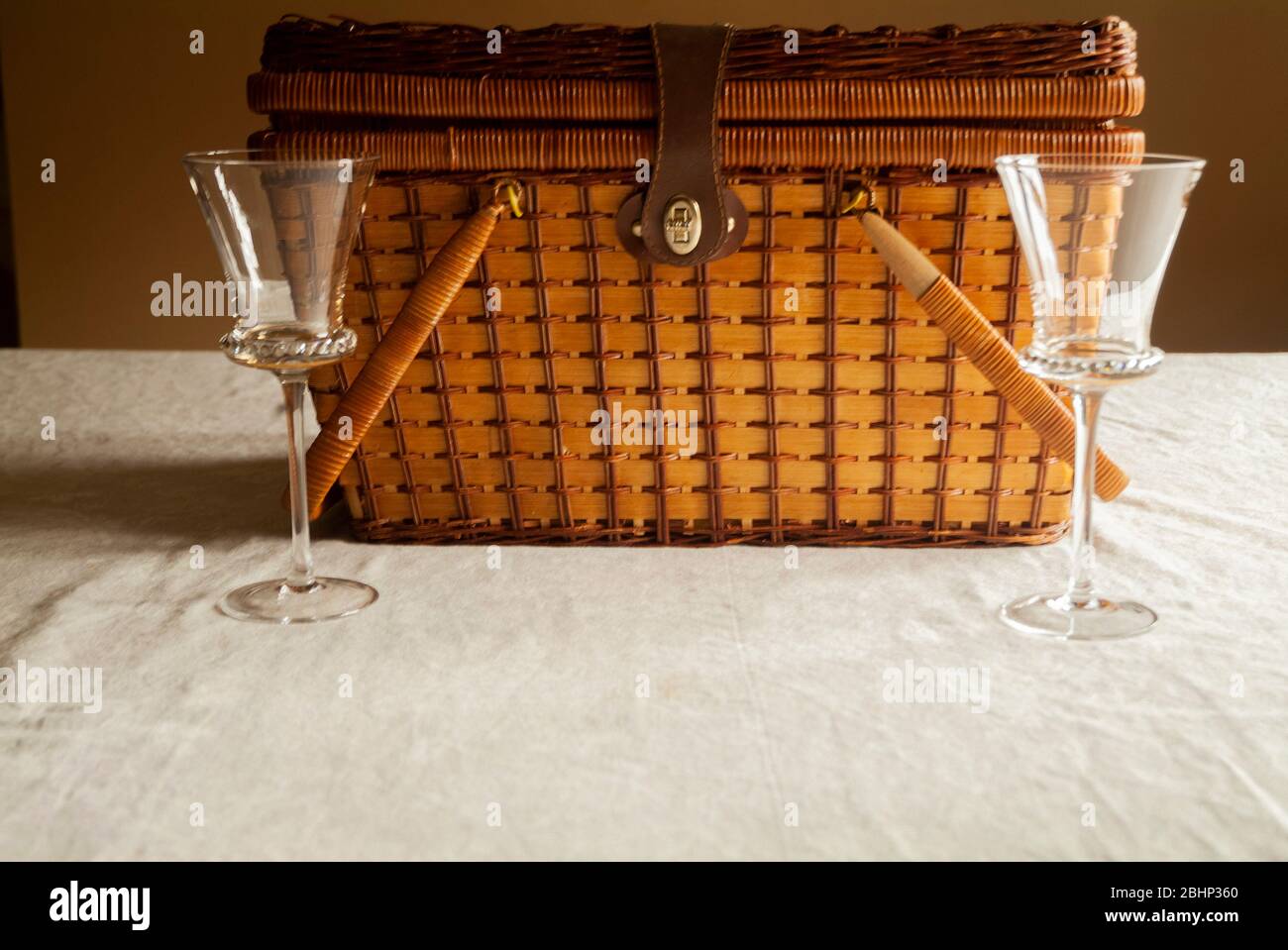 DATE NIGHT: Two wine glasses stand side by side in front of a picnic basket on a kitchen table. Stock Photo
