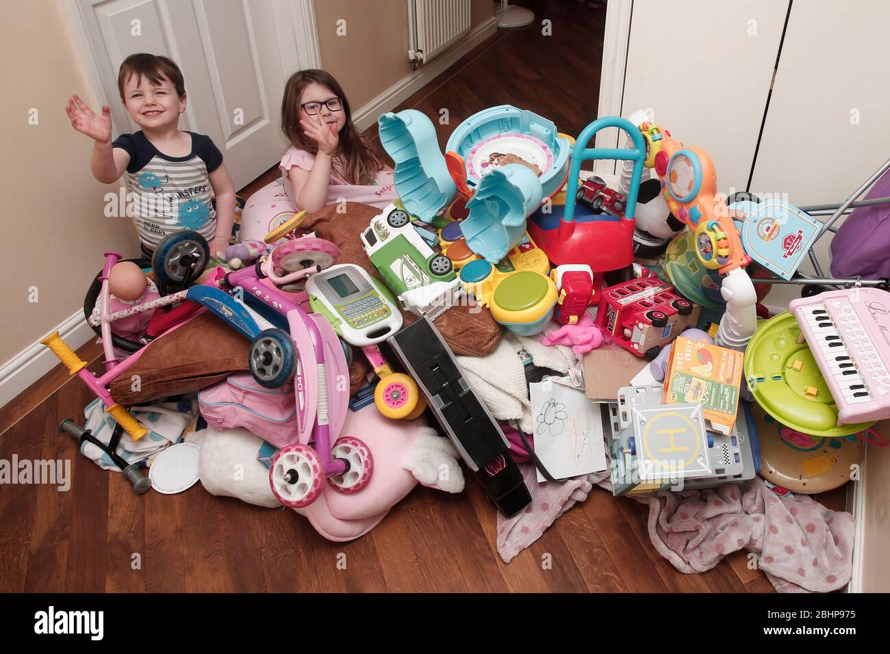 Two siblings surrounded by huge pile of children's toys at home Stock Photo