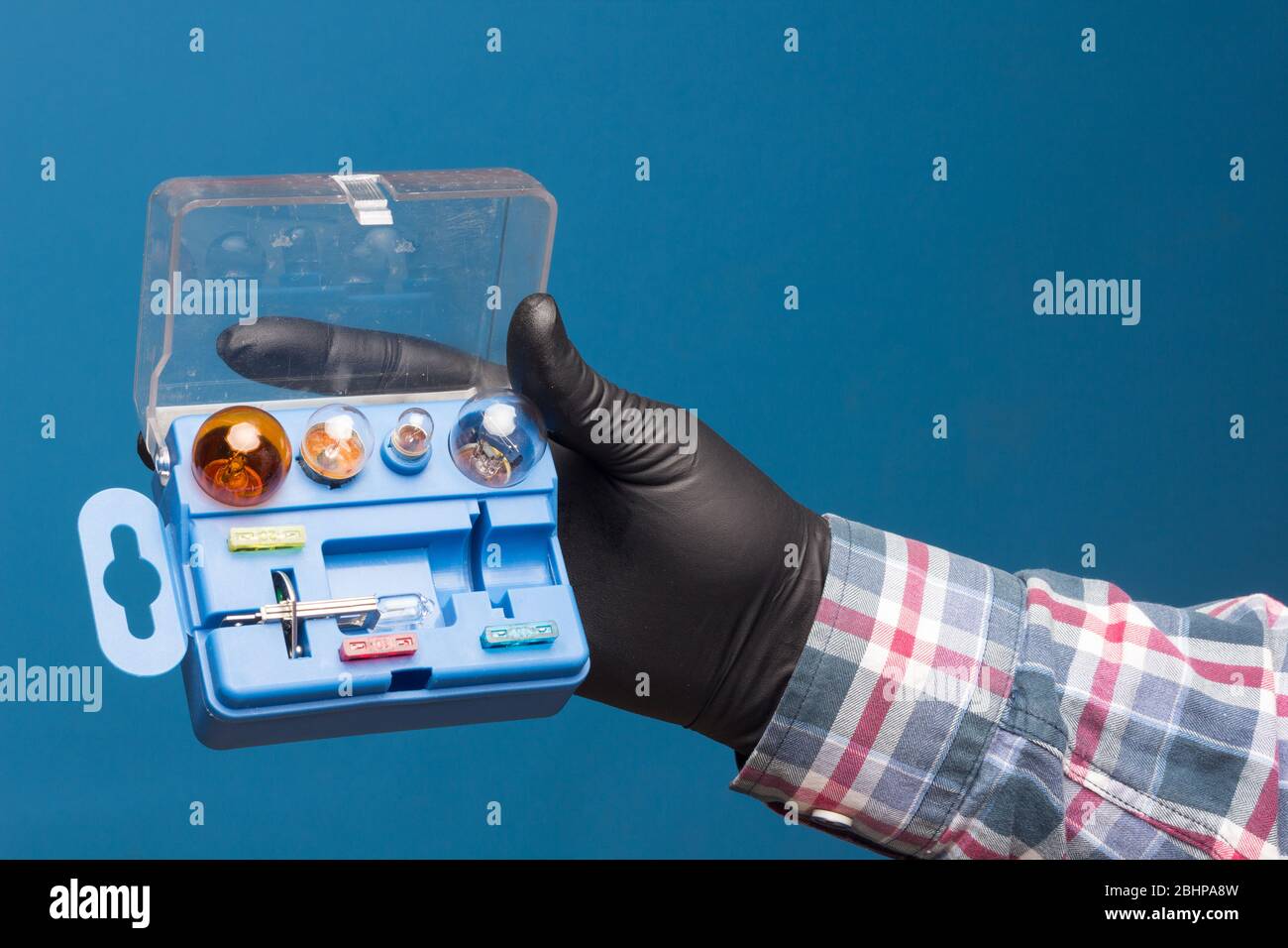 Lights and mandatory replacement material for cars in a plastic box and on hand with black glove and blue background Stock Photo