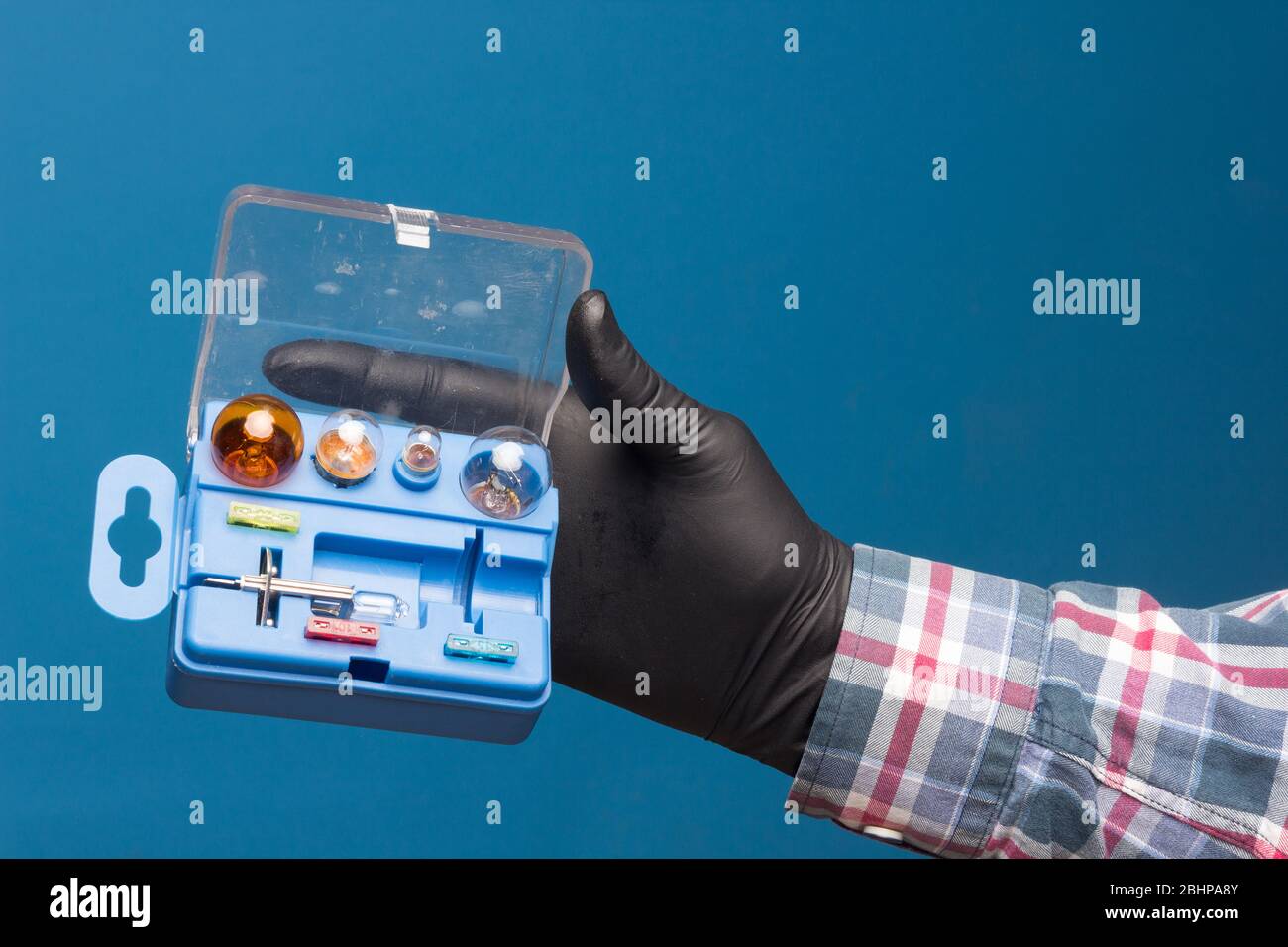 Lights and mandatory replacement material for cars in a plastic box and on hand with black glove and blue background Stock Photo