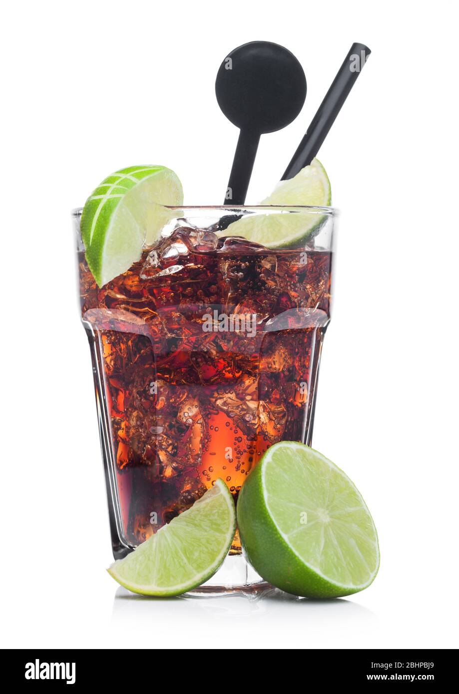 Cuba Libre Cocktail in glass with ice cubes and slices of lime with black straw and stirrer on white background with raw limes Stock Photo