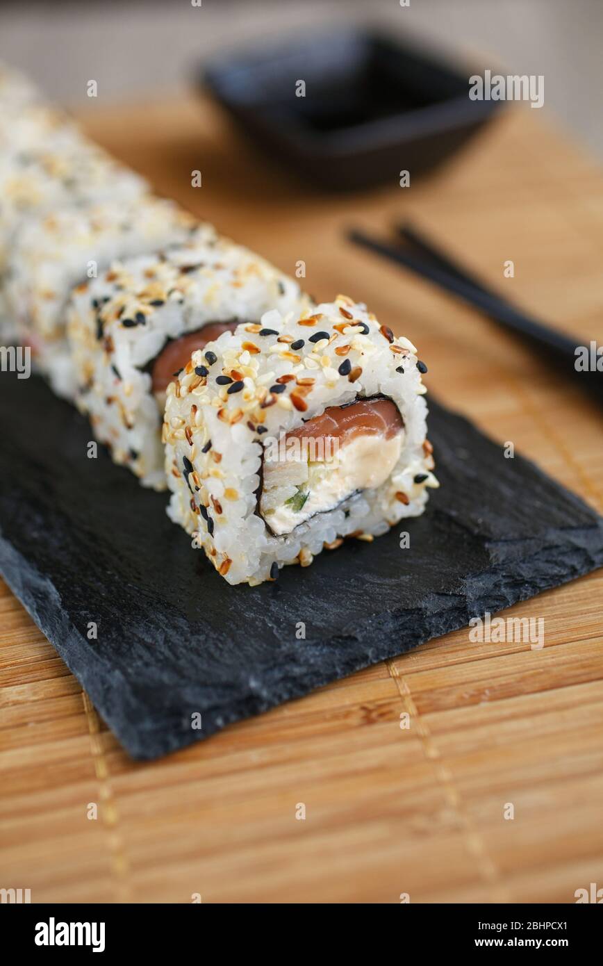 Japanese sushi rolls sprinkled with sesame seeds on a black stone board. Stock Photo