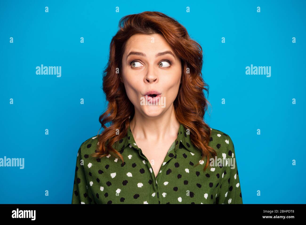Closeup photo of pretty curly shocked lady open mouth listen good news look interested side empty space wear green dotted office shirt isolated bright Stock Photo