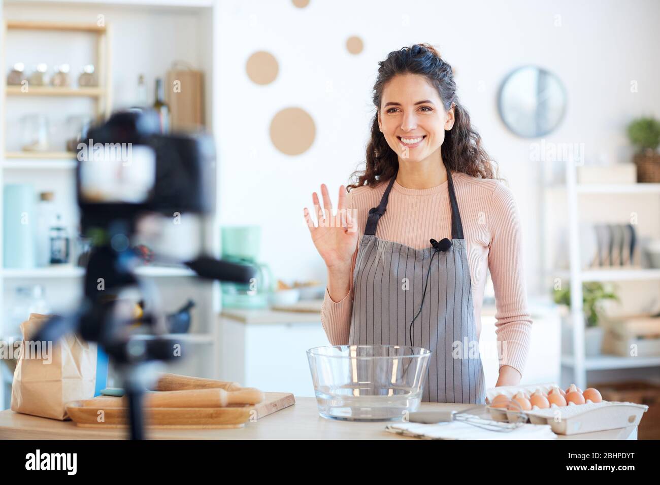 Beautiful Caucasian woman wearing apron starting her food blog video with greeting her viewers Stock Photo