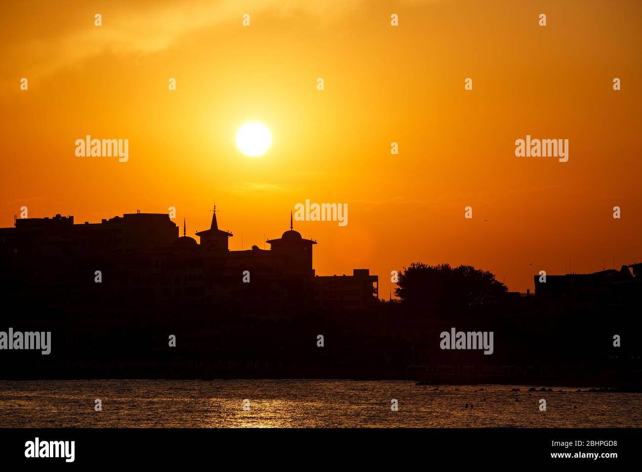 Golden sunset on the beach. Silhouette of the city. Beautiful architecort by the sea on the background of the sunset. Stock Photo