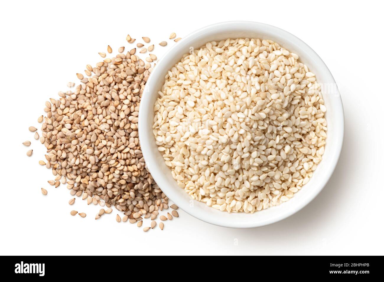 Peeled sesame seeds in a white ceramic bowl next to a pile of unpeeled sesame seeds isolated on white. Top view. Stock Photo