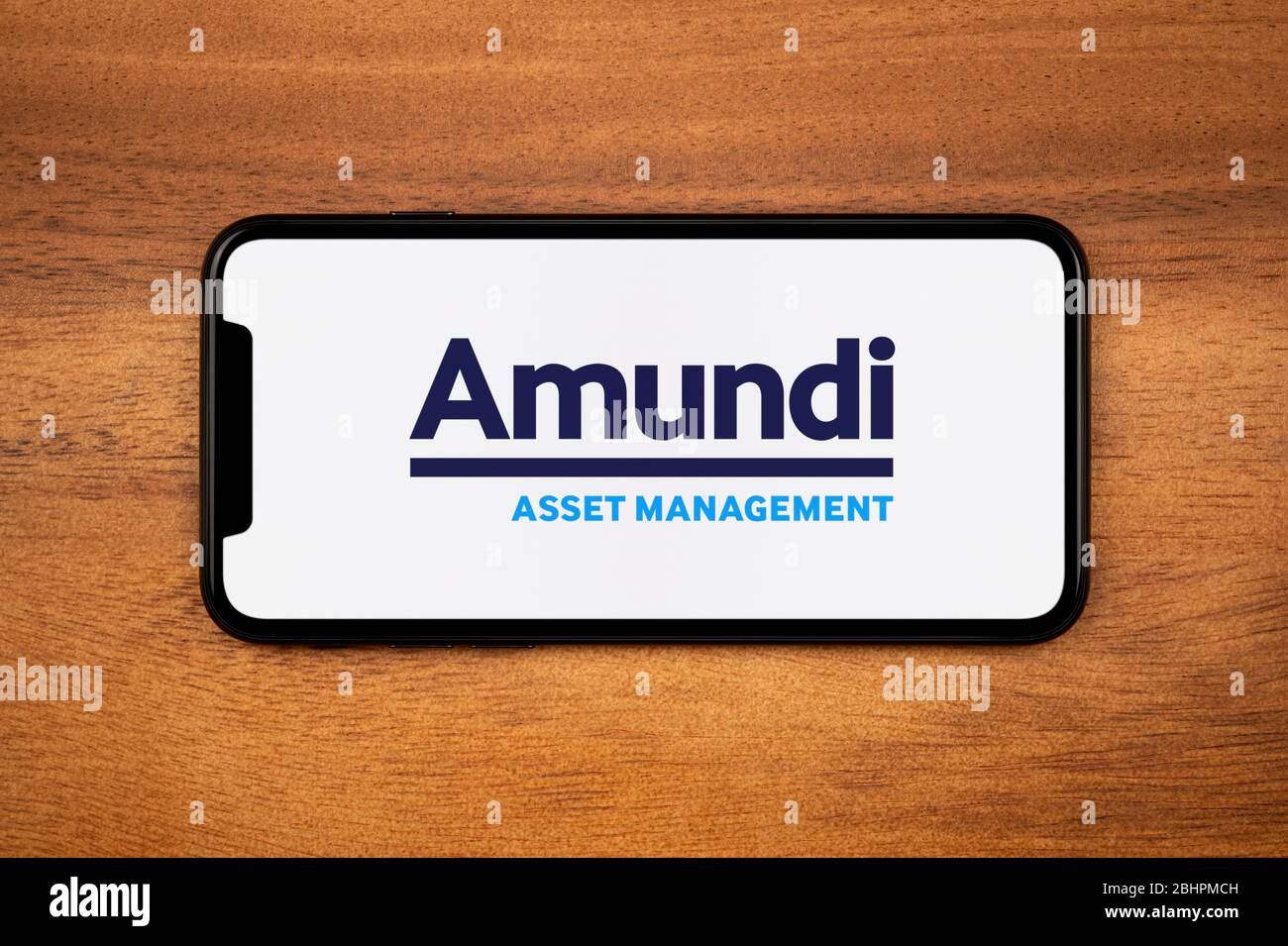 A smartphone showing the Amundi Asset Management logo rests on a plain wooden table (Editorial use only). Stock Photo