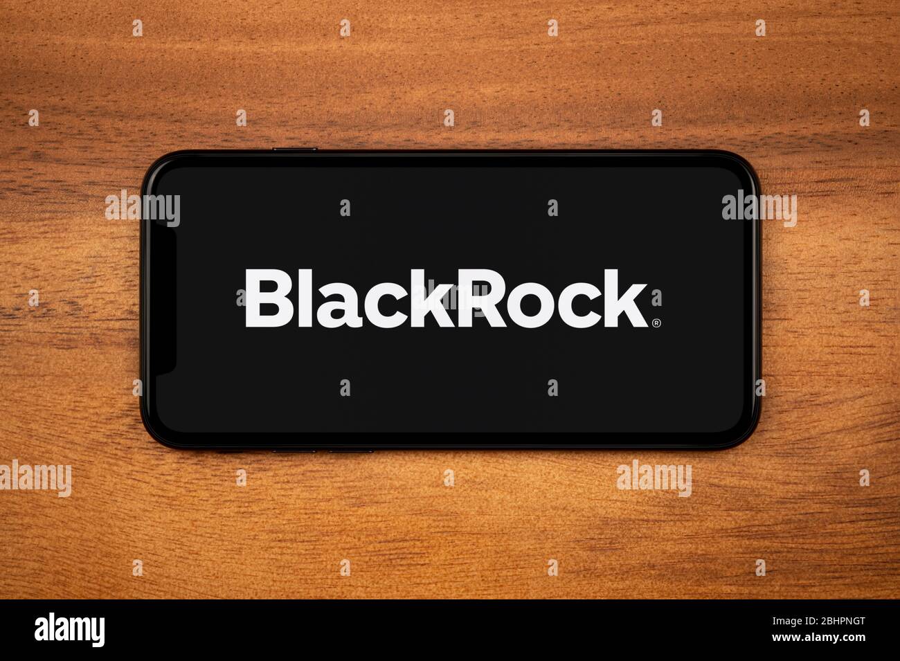 A smartphone showing the BlackRock logo rests on a plain wooden table