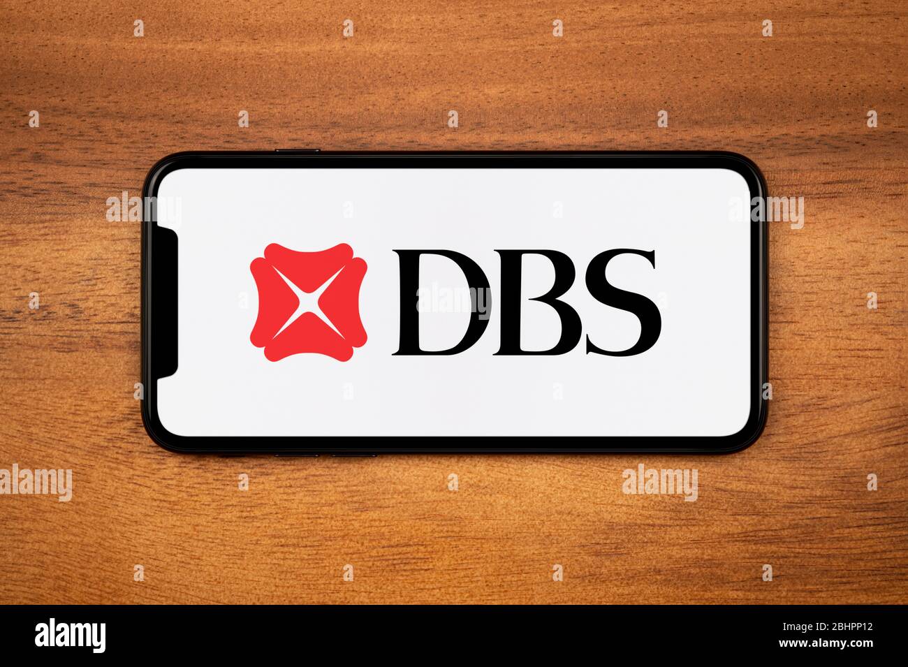 A smartphone showing the DBS Bank logo rests on a plain wooden table (Editorial use only). Stock Photo