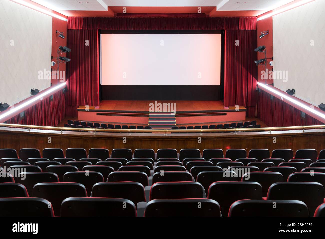 inside of movie theatre with vacant seats and the red curtains drawn open to reveal an empty stage viewed from the rear 2BHPRF6