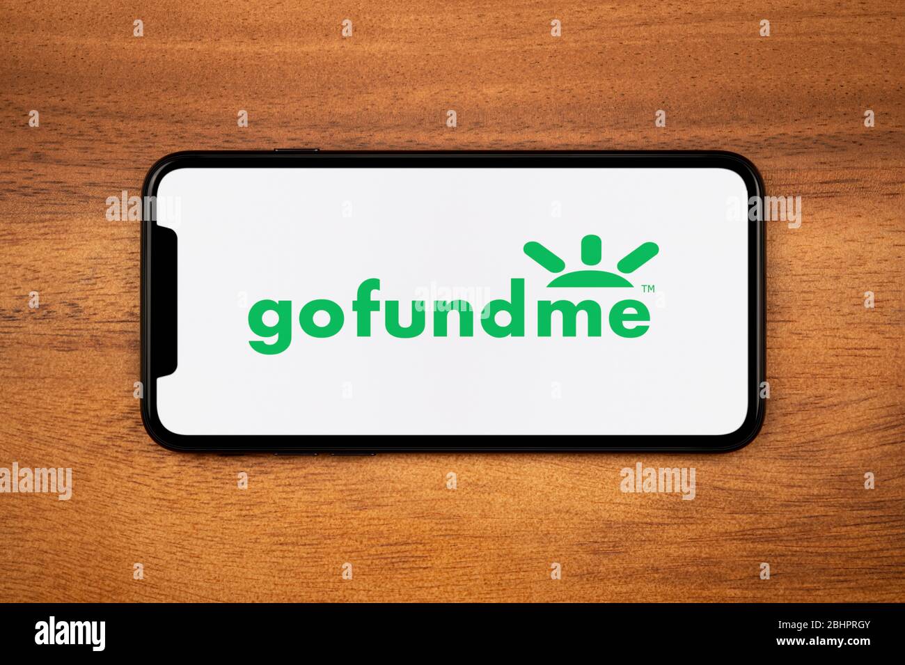 A smartphone showing the Gofundme logo rests on a plain wooden table (Editorial use only). Stock Photo