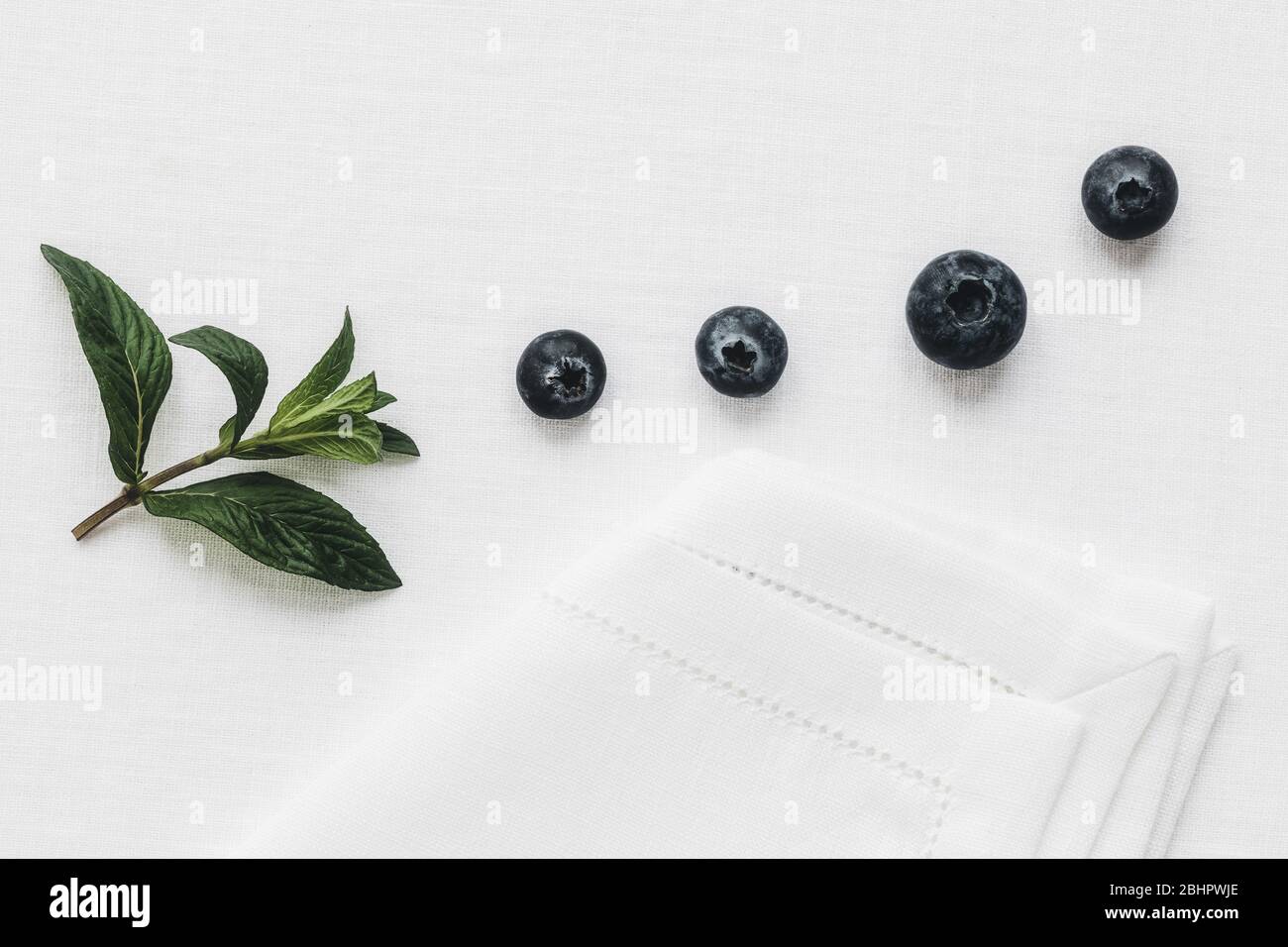 Fresh mint and Blueberry on a white linen tablecloth in the morning light. Stock Photo