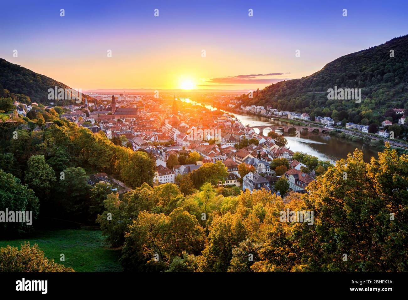 Travel shot: aerial view of Heidelberg, Germany, in beautiful sunset light, framed by colorful trees and gold and purple clear sky, with the Neckar ri Stock Photo