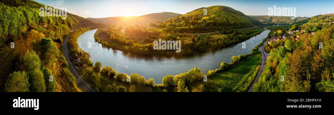 Panoramic aerial landscape shot of Neckar river, Germany, at a beautiful sunset, with clear sky and the vegetation being colorfully lit, a road follow Stock Photo