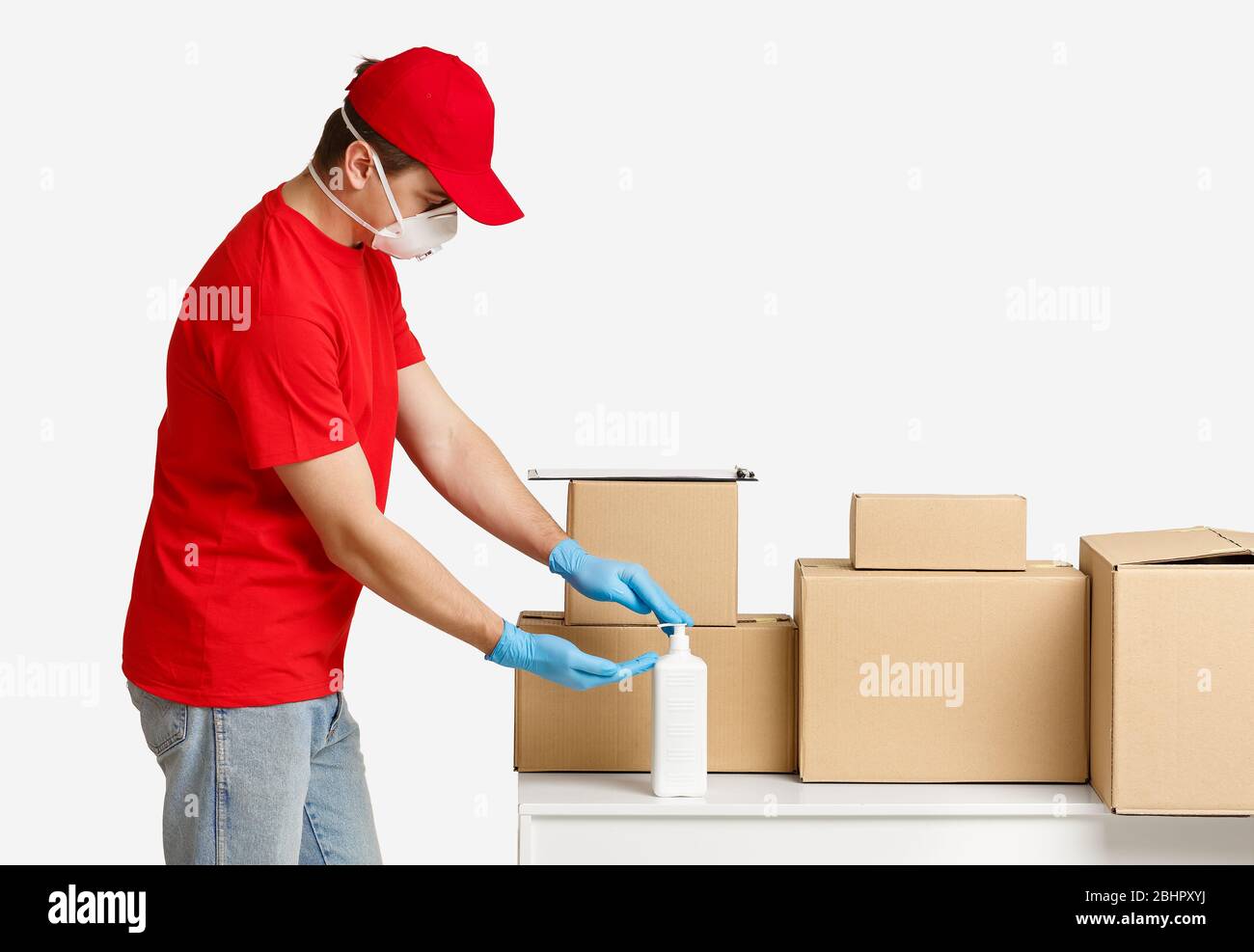 Courier in red uniform disinfects hands near boxes Stock Photo