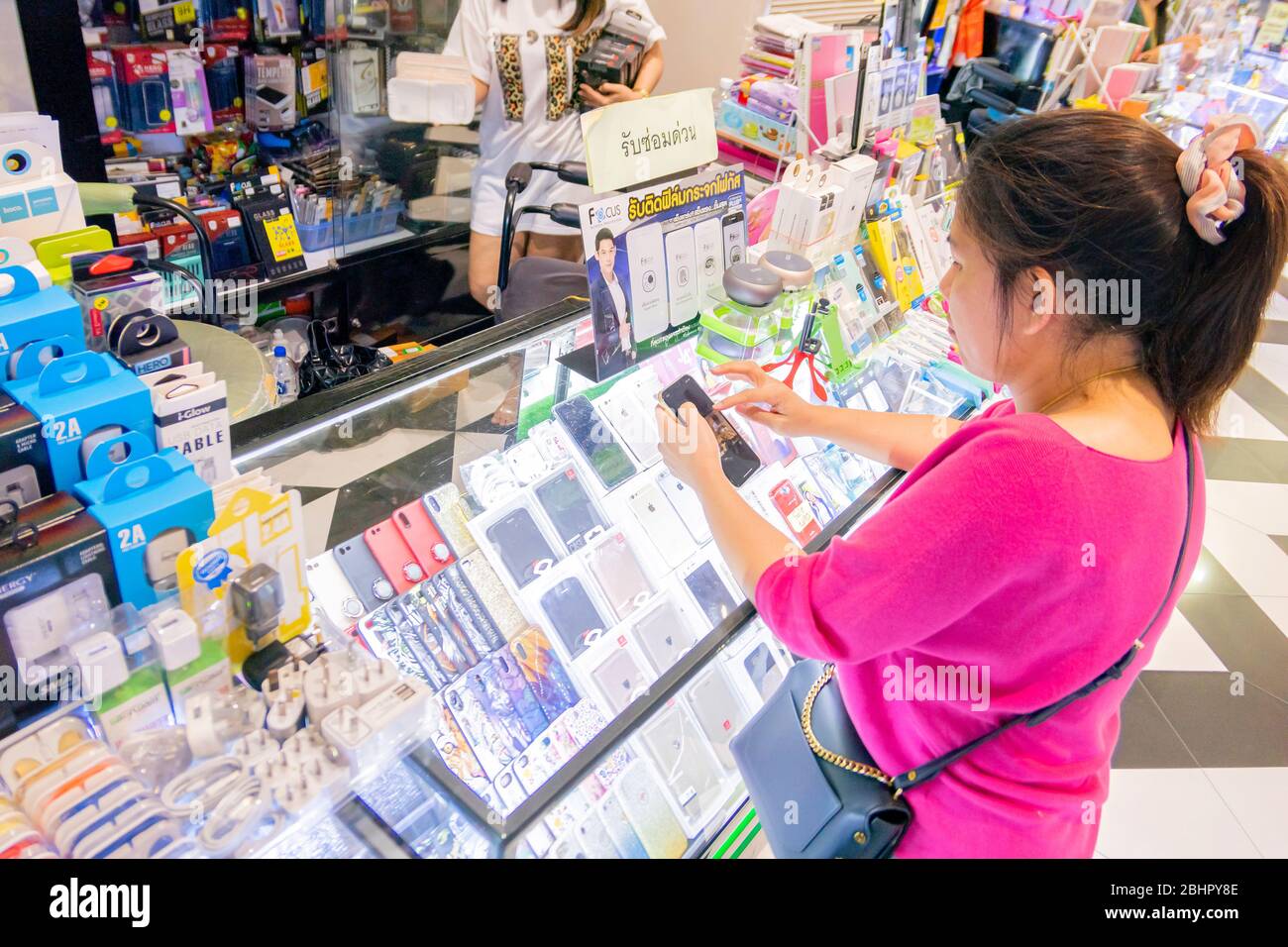 An Asian woman in pink shirt is waiting for changing her mobile phone protection film at the phone accessories shop in Village market in Huahin, Thail Stock Photo