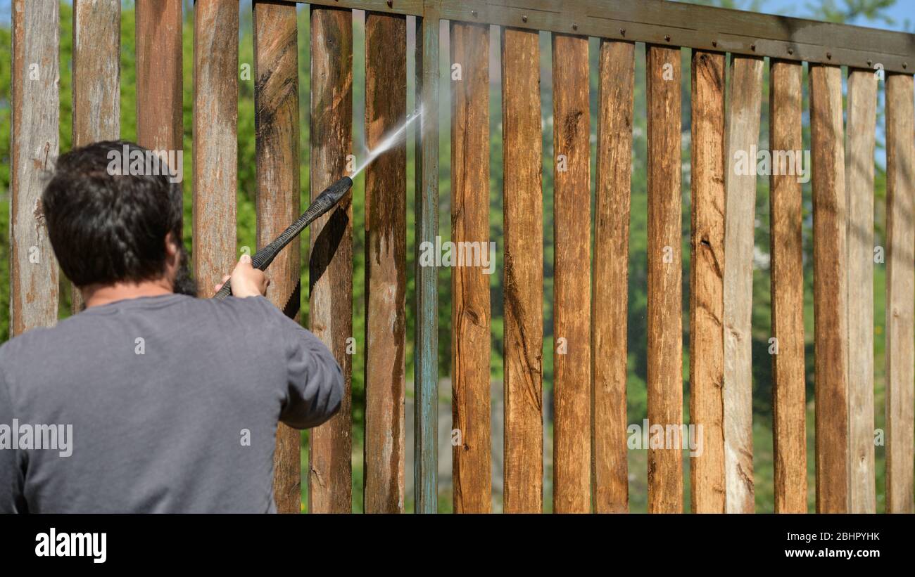 Unrecognizable man cleaning a wooden gate with a power washer. High ...