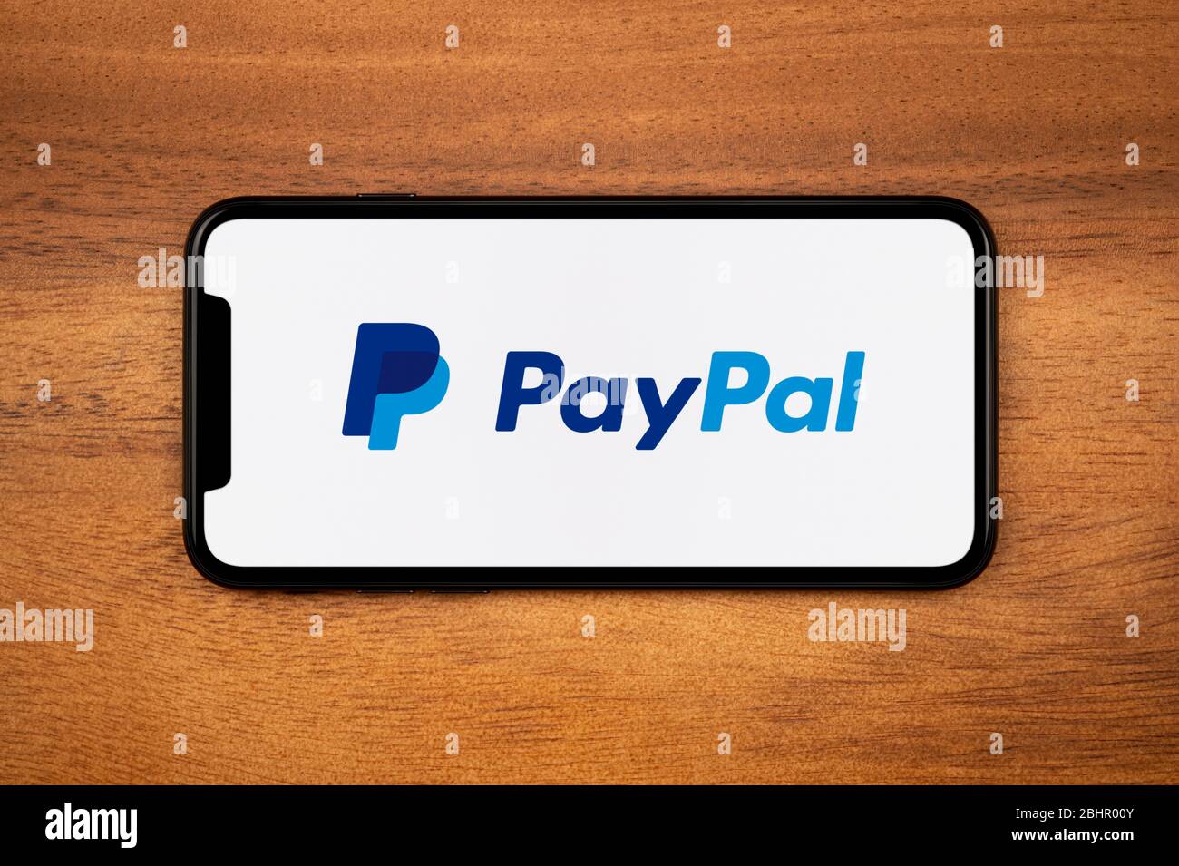 A smartphone showing the PayPal logo rests on a plain wooden table (Editorial use only). Stock Photo