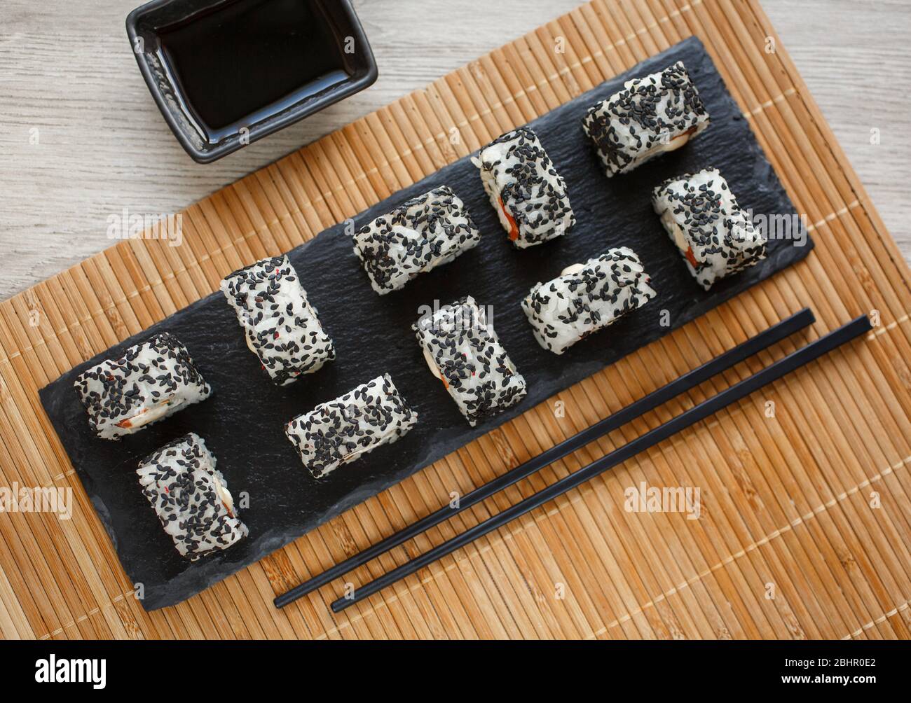 Minimalism and sophistication: delicious salmon and avocado sushi covered with black sesame seeds. Served with ginger and wasabi on a black stone. Stock Photo