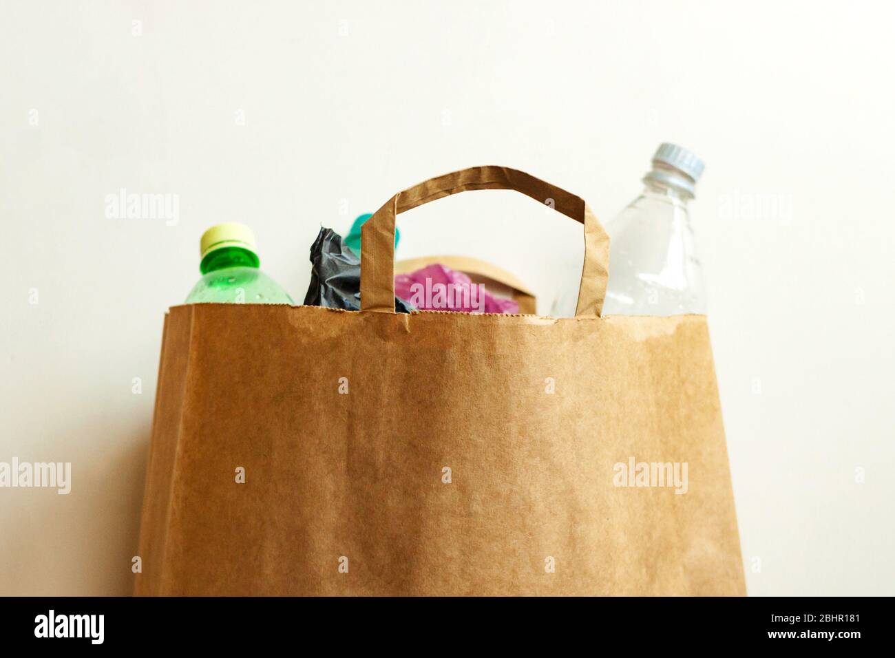 Empty used plastic bottles, bags in brown paper bag, sorting waste for recycling on light background Stock Photo