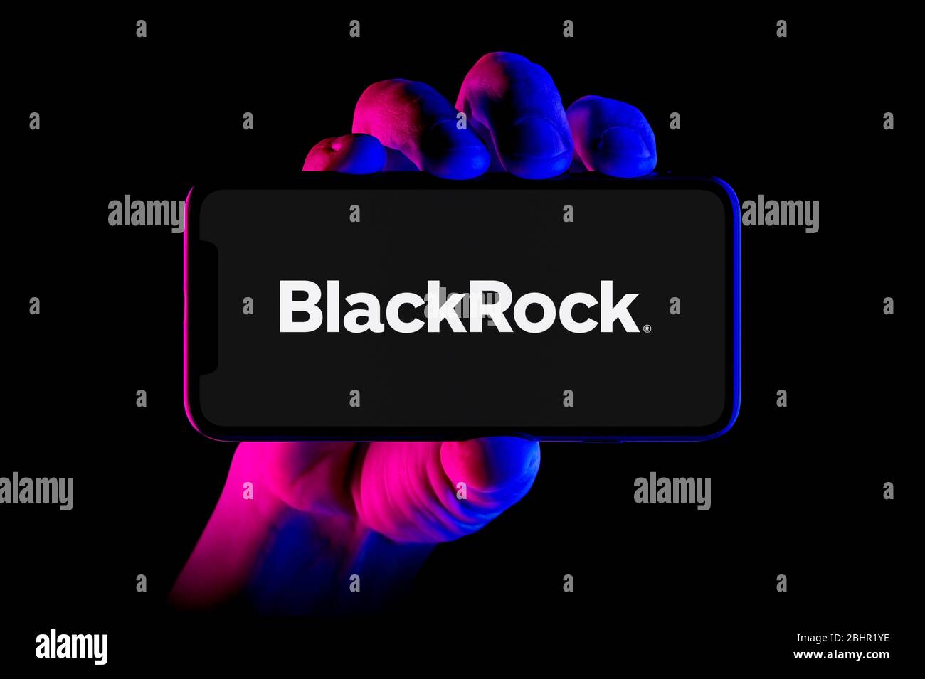 A smartphone displaying the BlackRock logo is held by a hand shot on a black background (editorial use only). Stock Photo