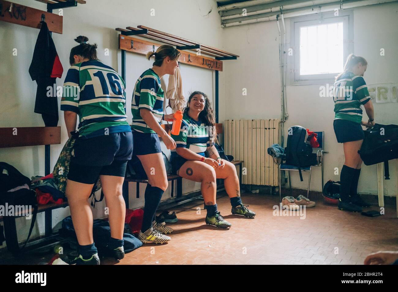 Four women wearing blue, white and green rugby shirts in a dressing