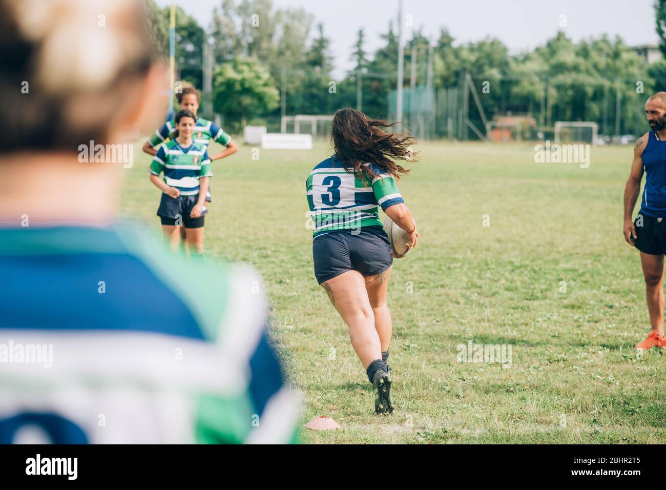 Women wearing blue, white and green rugby shirts on a training pitch
