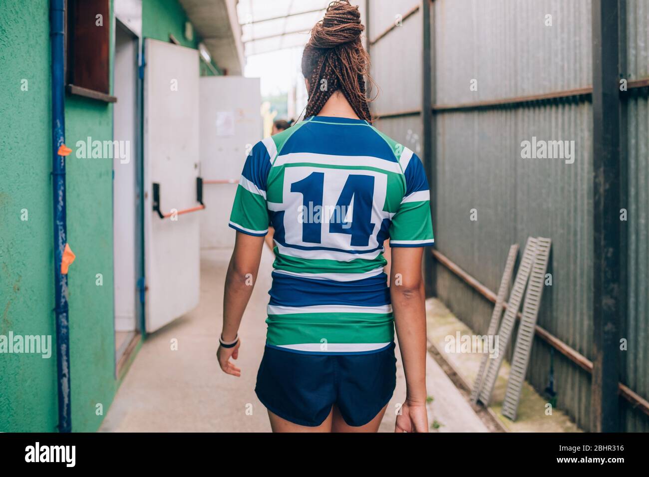 Rear view of a woman wearing a green, blue and white rugby shirt walking towards the dressing rooms. Stock Photo